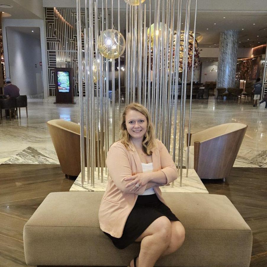 Amanda smiling in a luxurious, brightly lit resort lobby featuring marble flooring and a modern vertical rod light fixture.